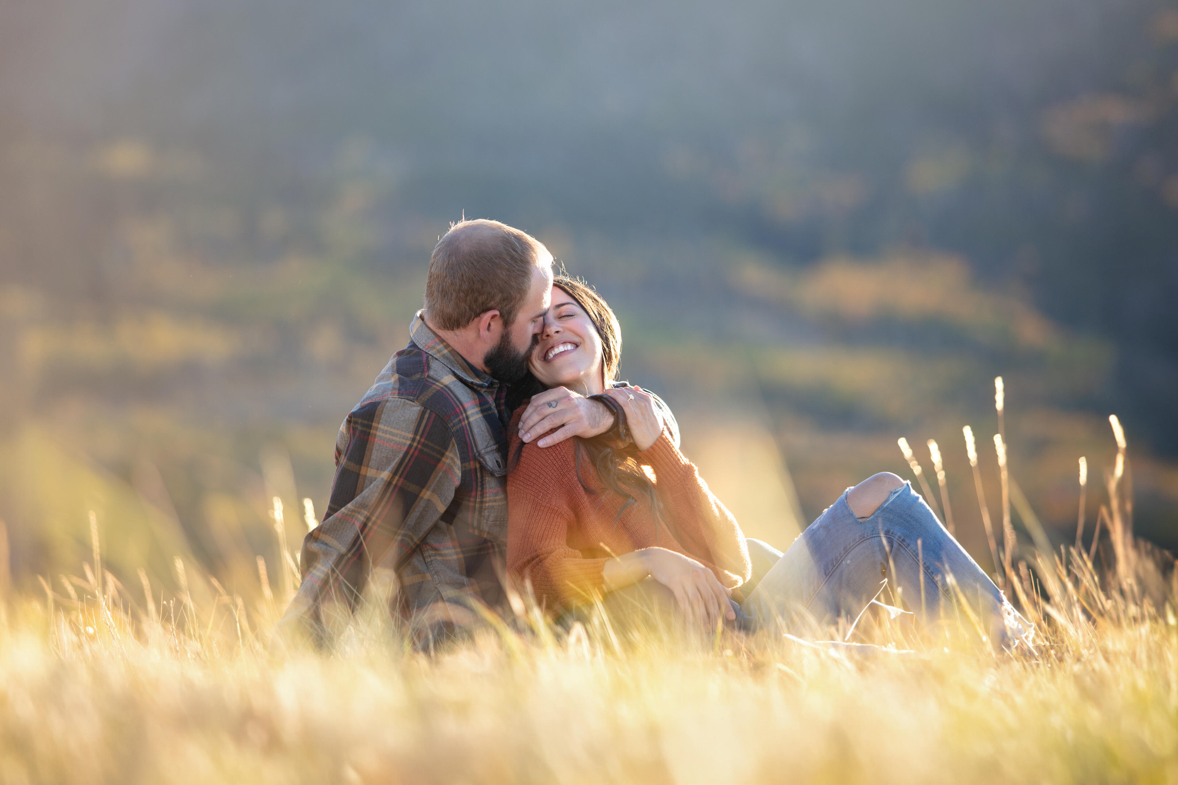 Couple laughing and embracing in a sunlit mountain meadow during a golden hour photography session in Breckenridge, Colorado